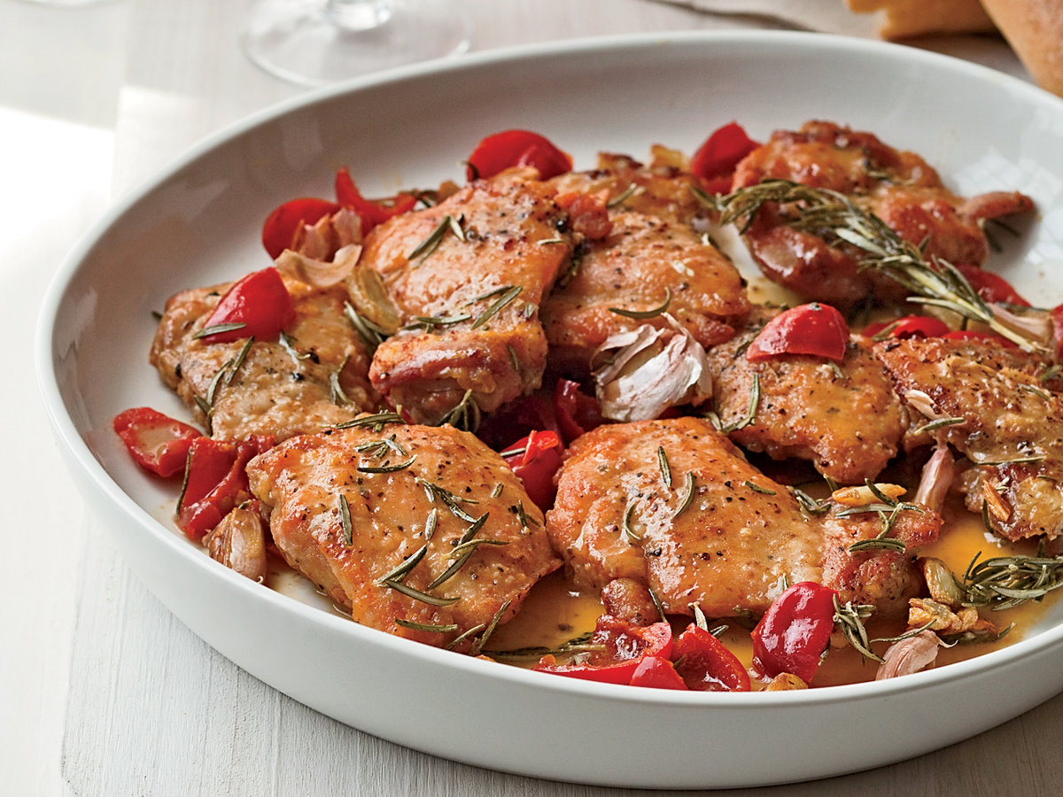 A plate of herb-seasoned cooked chicken with roasted garlic and cherry tomatoes.