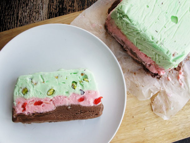 Slice of pistachio and cherry ice cream cake on a white plate.