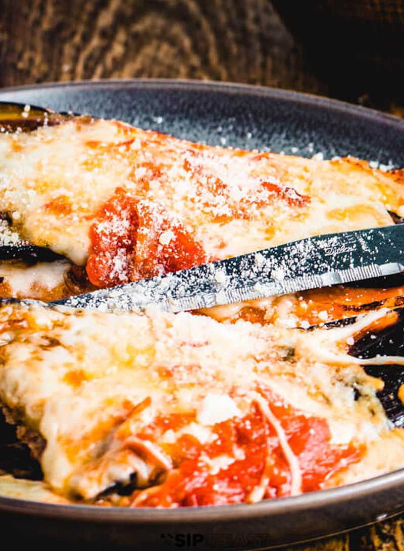 Close-up of cheesy pizza being sliced with a knife.