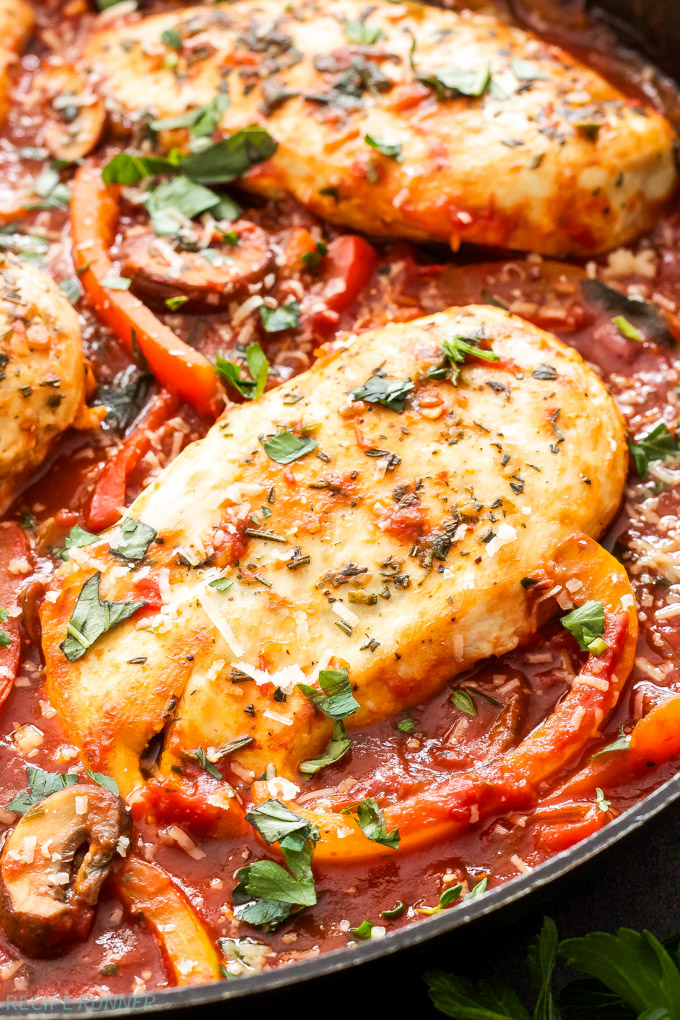 Close-up of a seasoned chicken breast cooked with tomatoes and herbs.