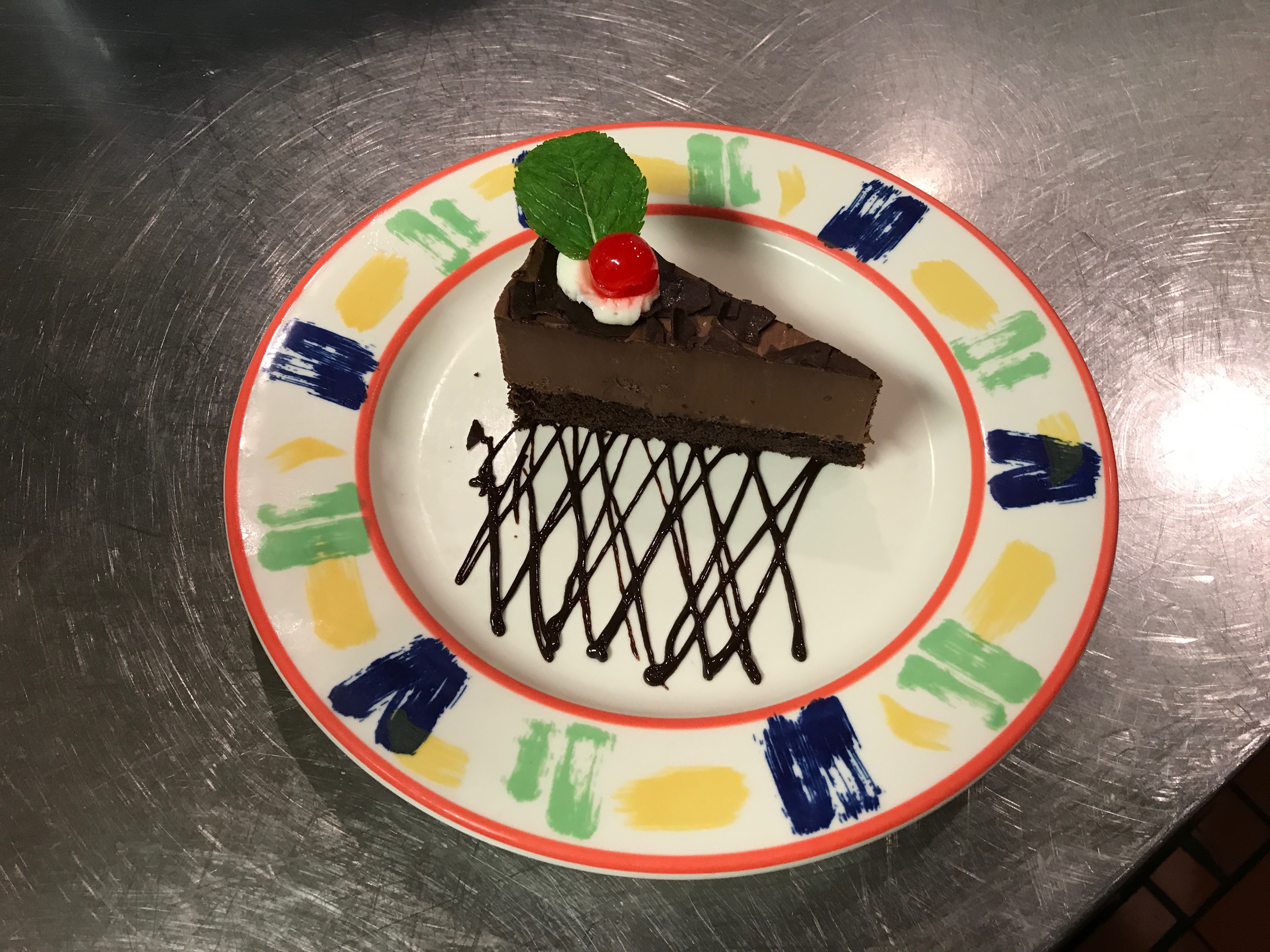 A slice of chocolate cheesecake with cherry and mint on a colorful plate.