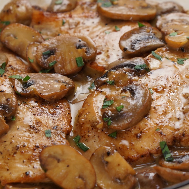 Close-up of cooked chicken breasts topped with sautéed mushrooms and herbs.