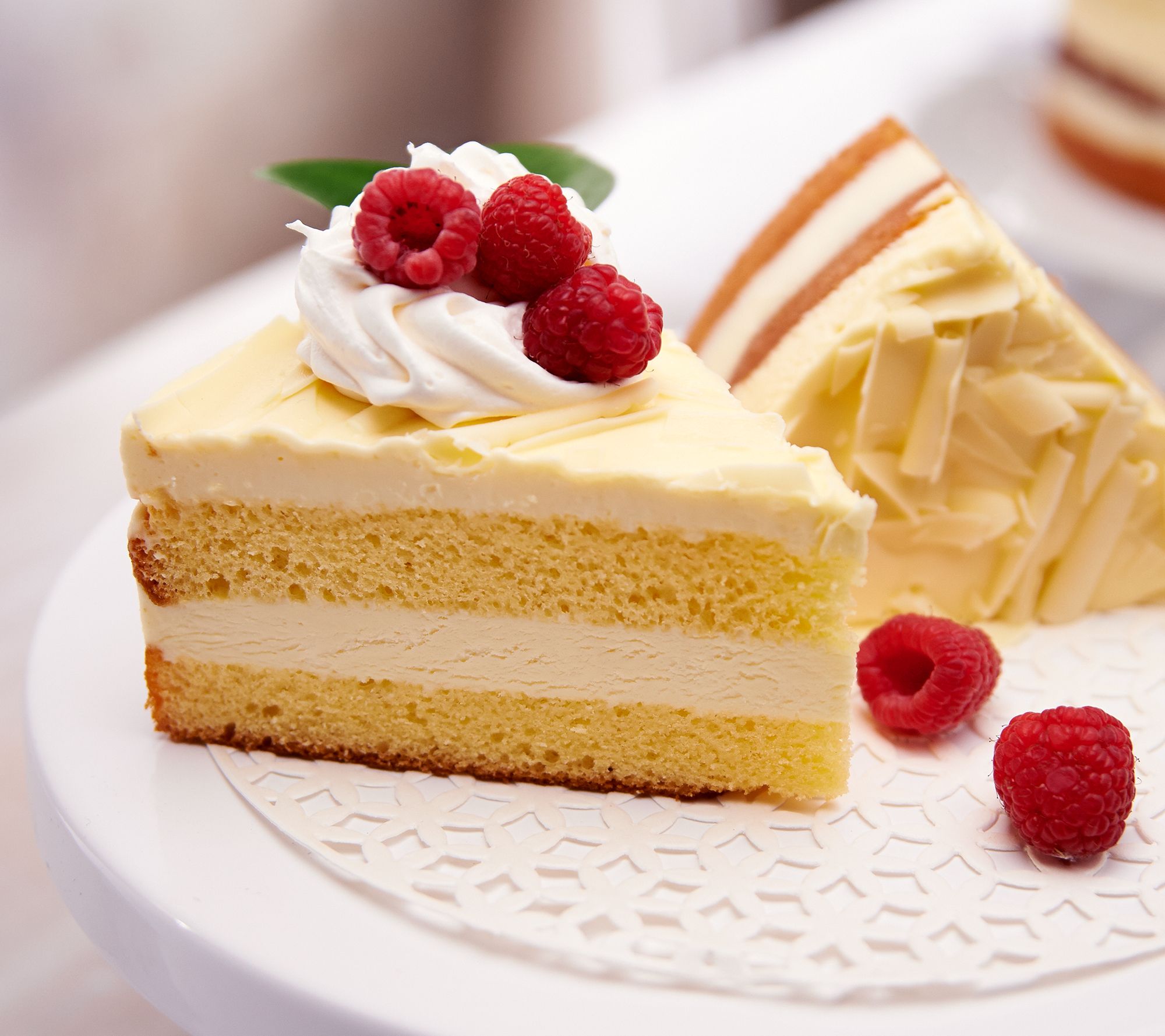 Two slices of creamy cake topped with raspberries on a white plate.