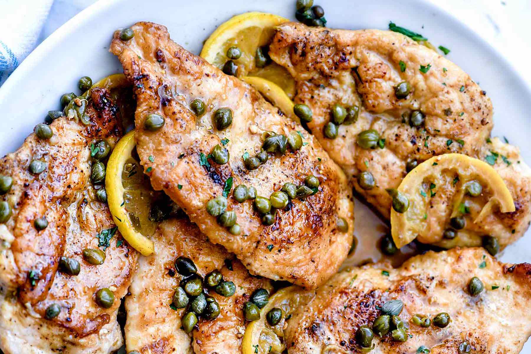 Grilled chicken breasts garnished with capers and lemon slices on a white plate.