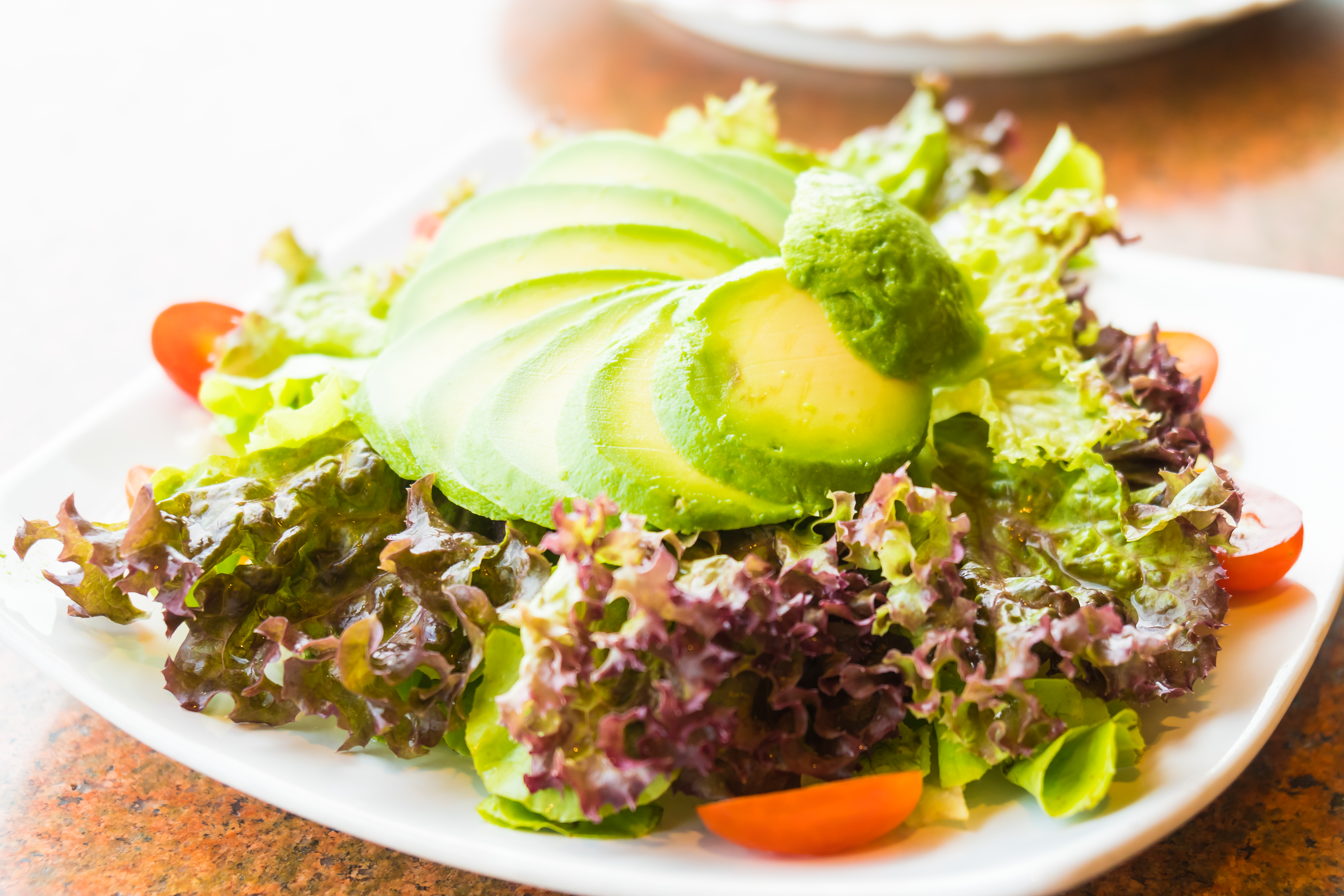 Fresh avocado slices on leafy green lettuce with cherry tomatoes.