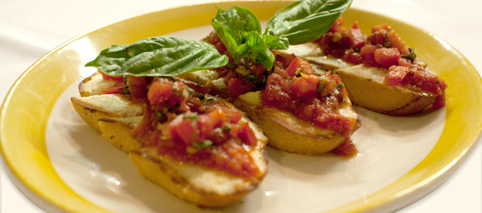 Bruschetta topped with tomato salsa and fresh basil leaves on a plate.