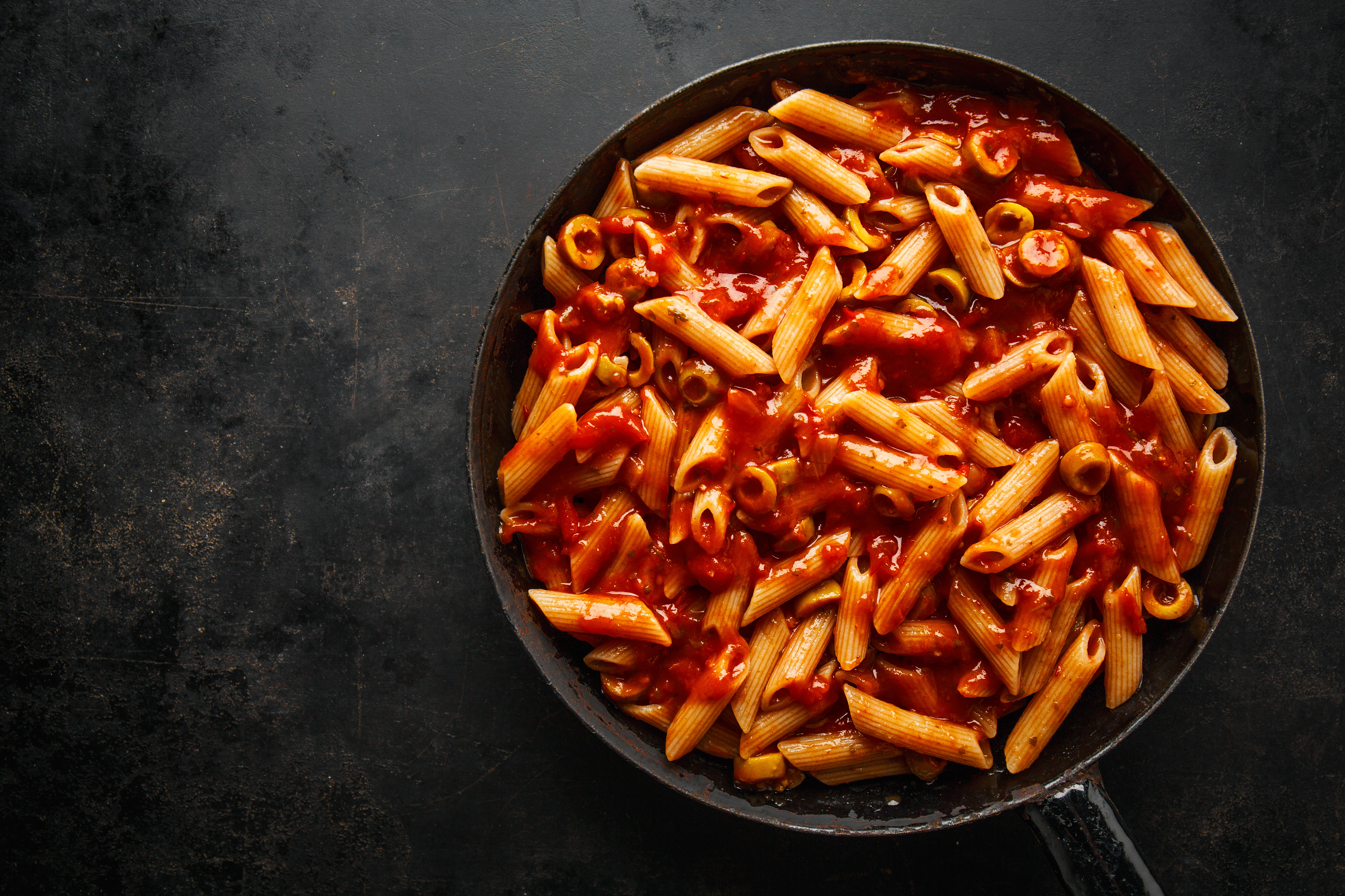 Penne pasta in rich tomato sauce in a black skillet.