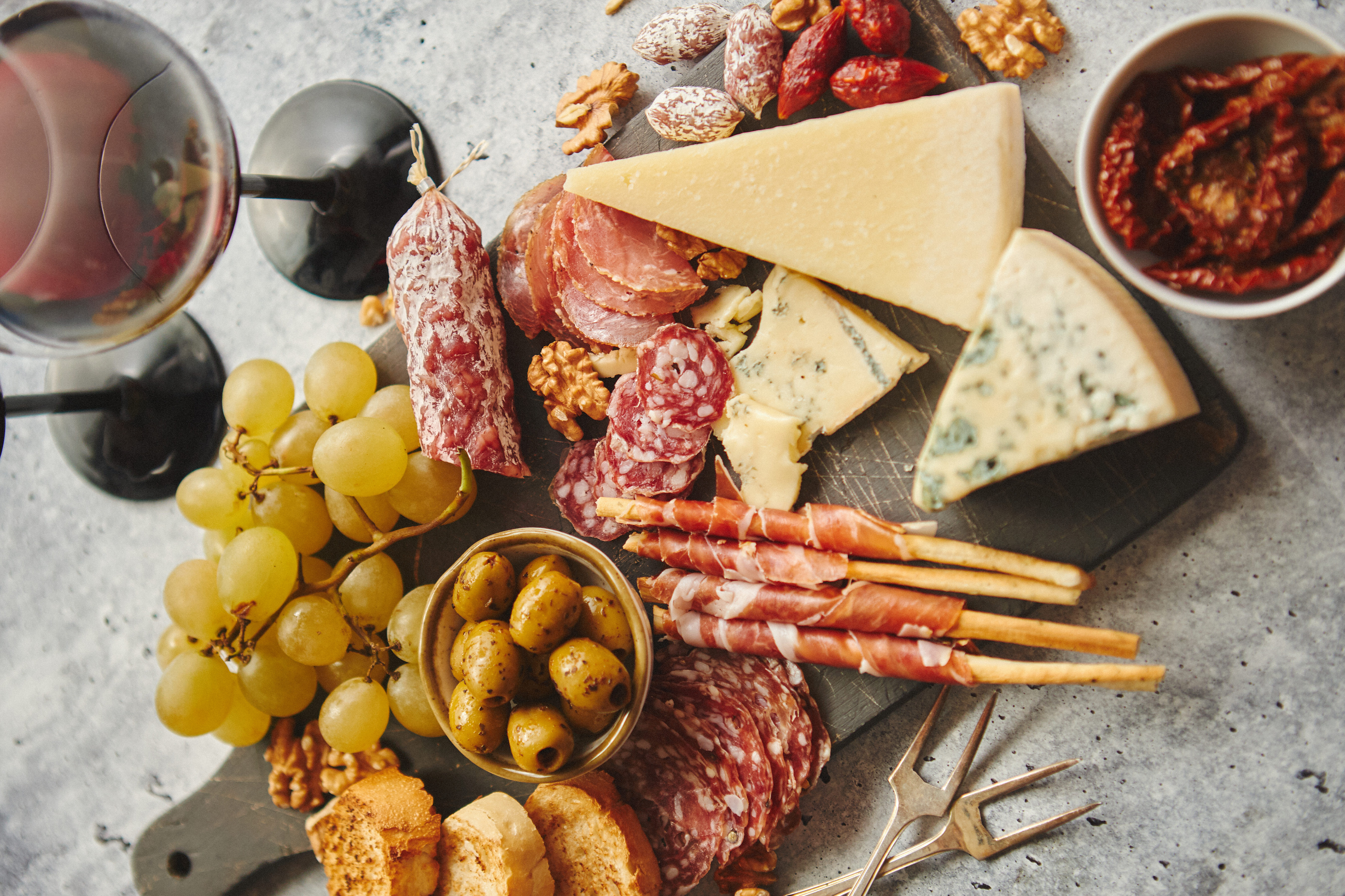 A charcuterie board with cheeses, meats, grapes, olives, and wine.