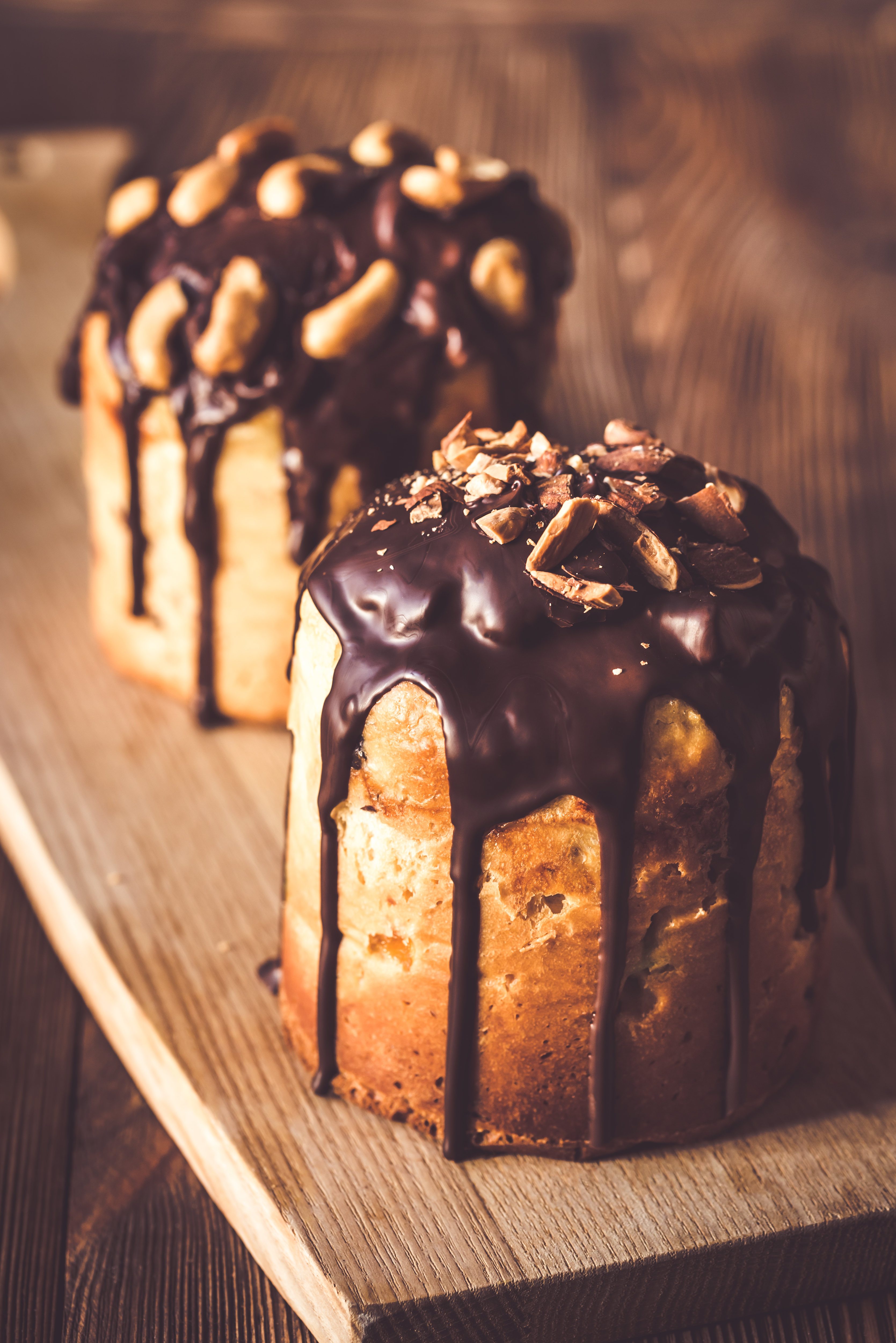 Chocolate-drizzled cake topped with chopped nuts on wooden surface.