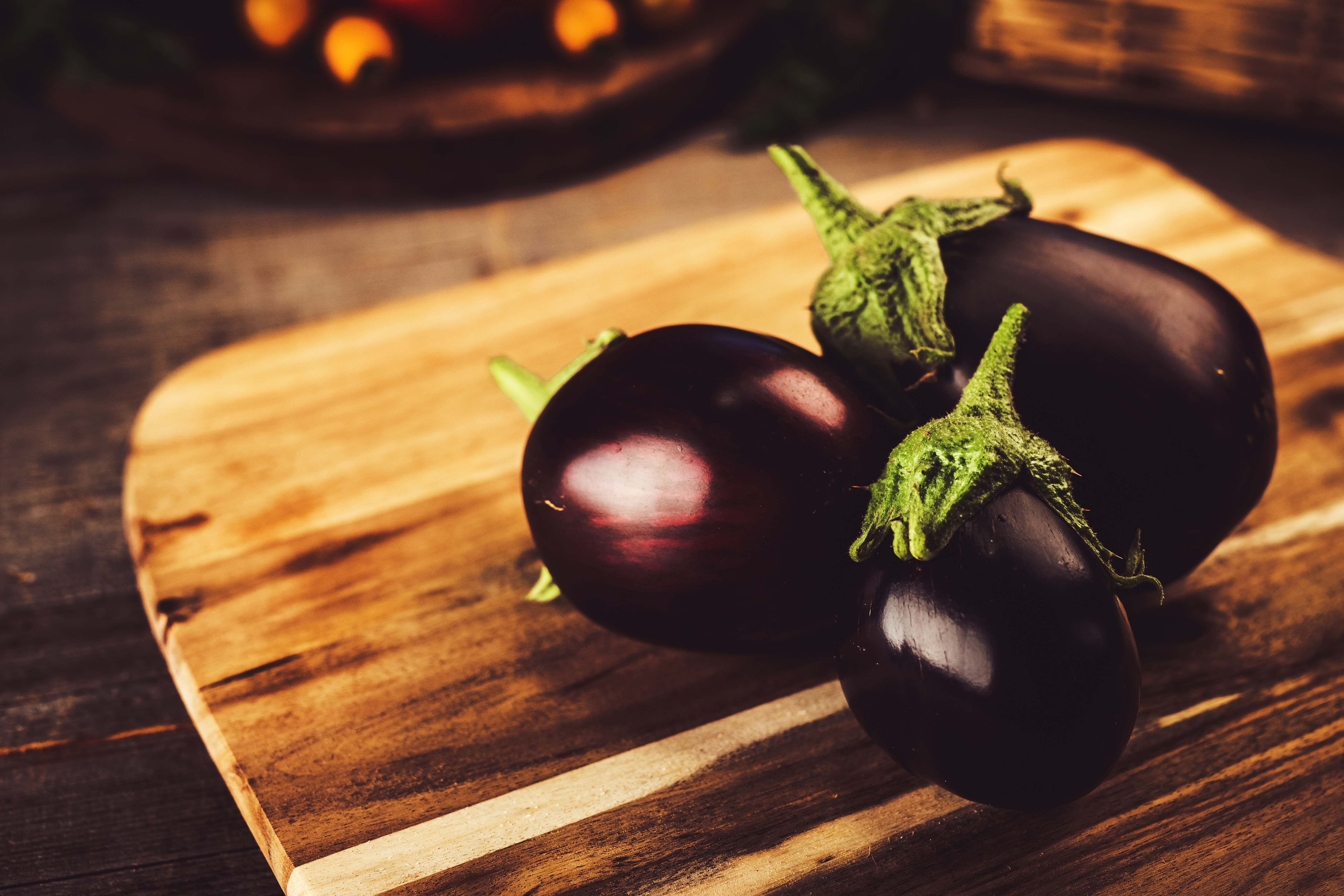 Three fresh eggplants on a wooden cutting board.