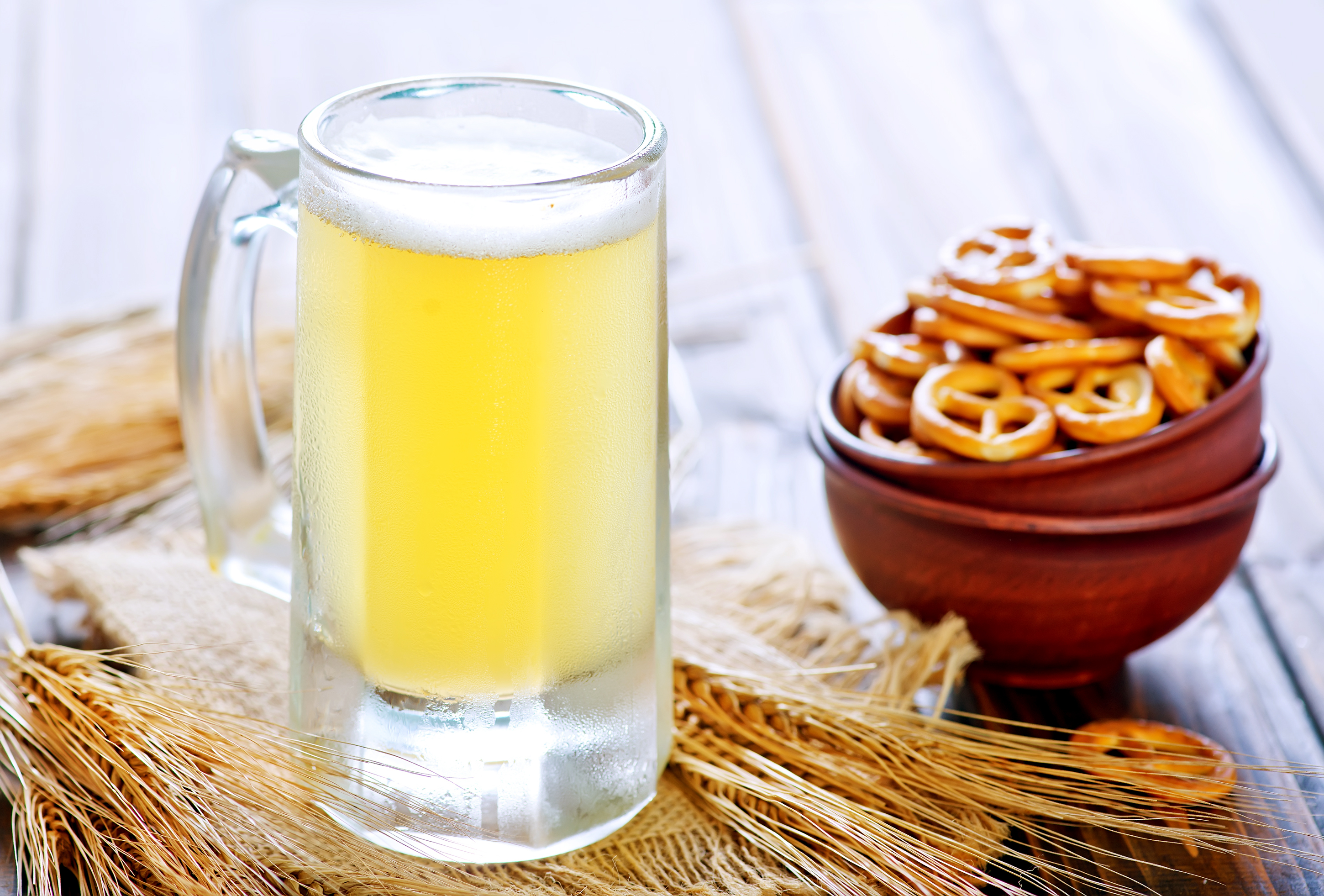 A frosty mug of beer with pretzels in wooden bowls on a rustic table.