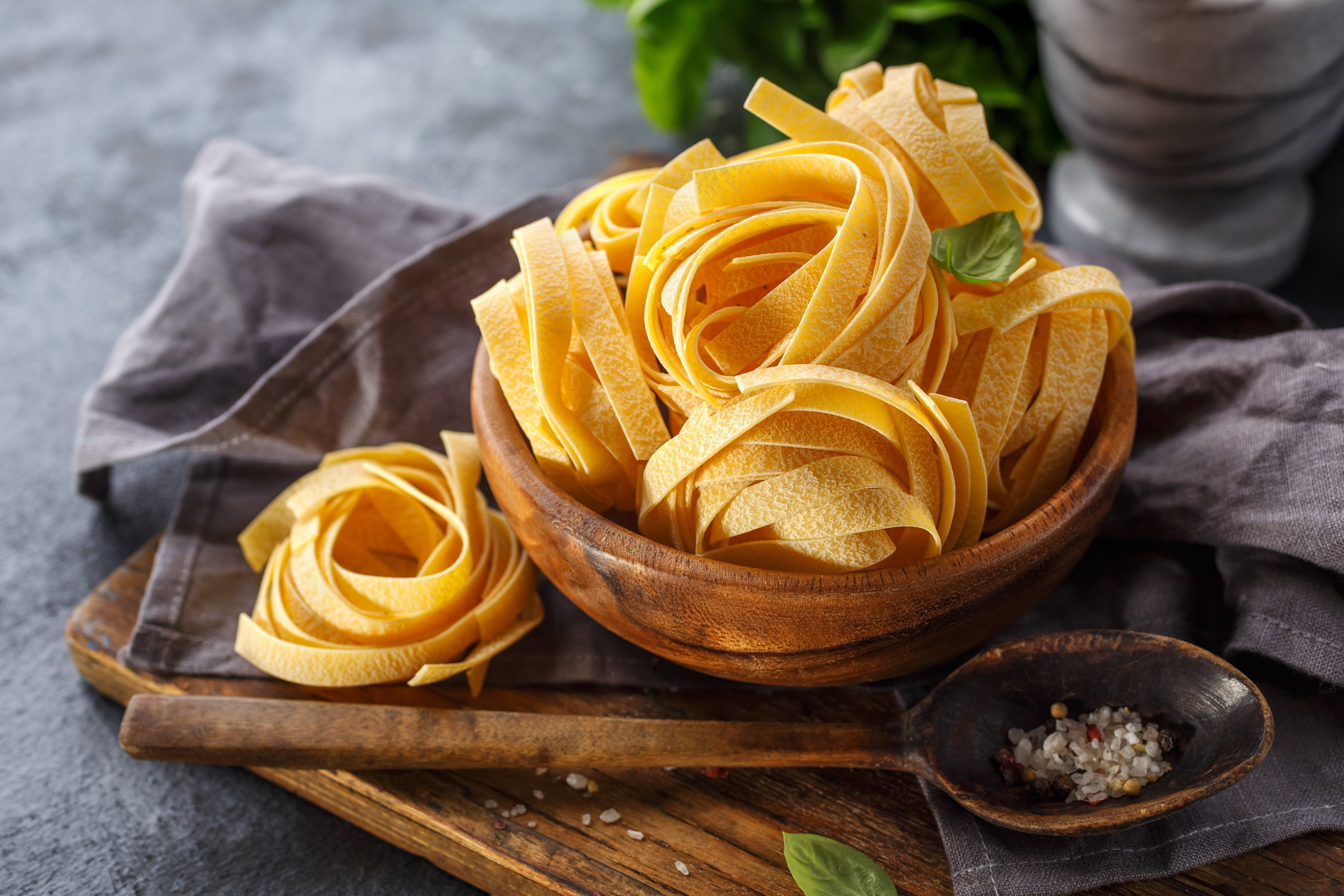 Wooden bowl filled with uncooked tagliatelle pasta nests on a rustic wooden board.
