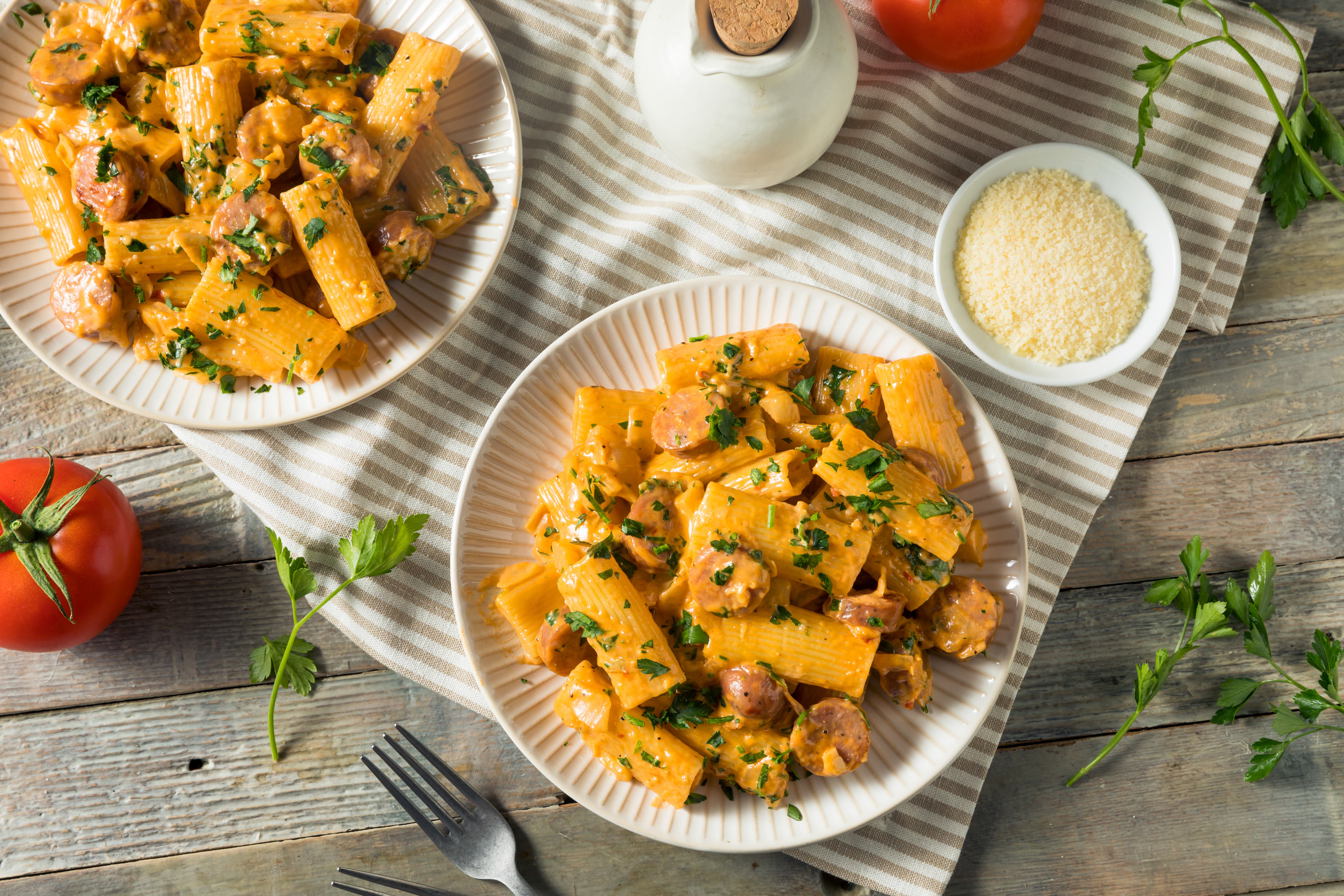 Two plates of creamy sausage pasta garnished with parsley.