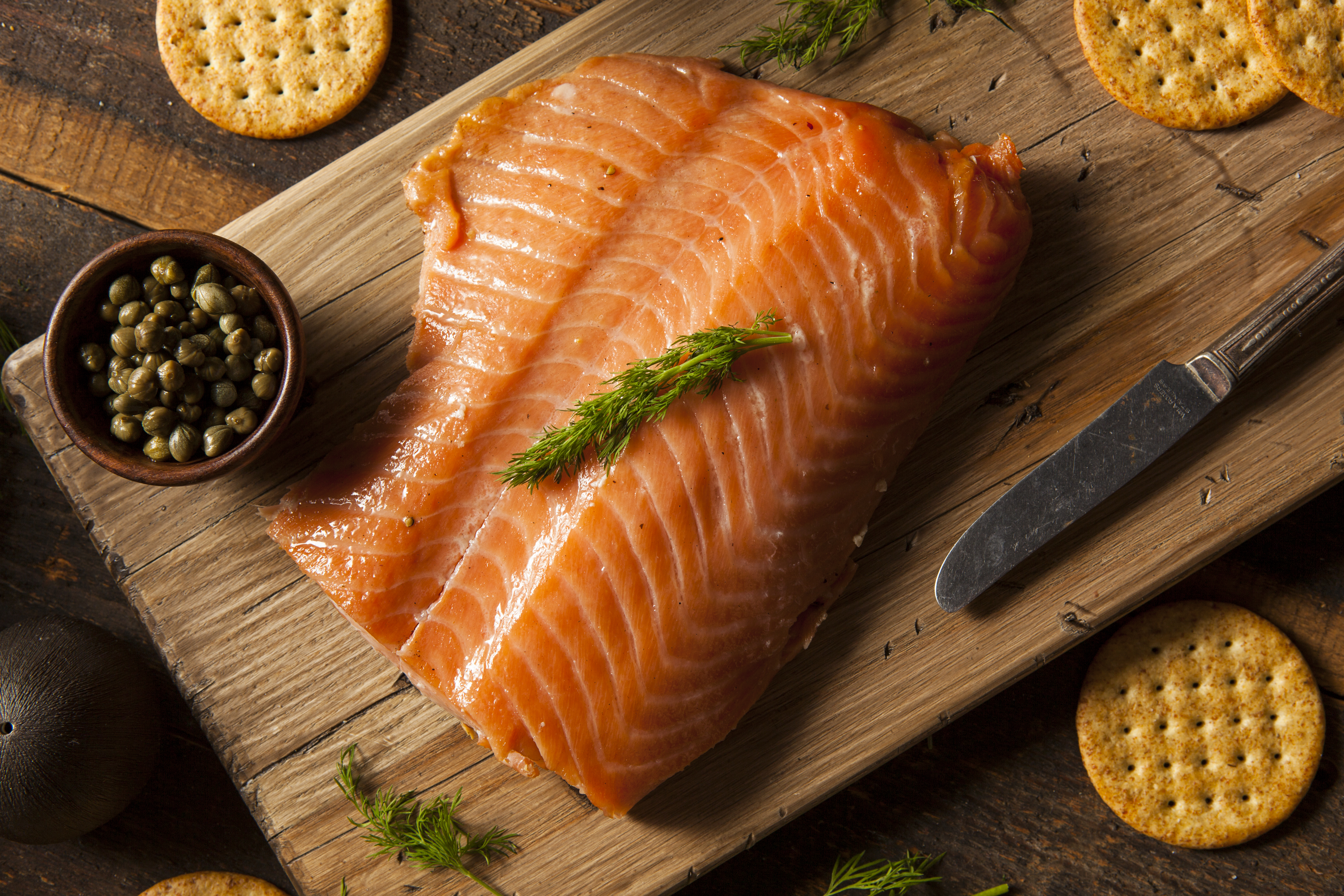Fresh salmon fillet on a wooden board with crackers and capers.