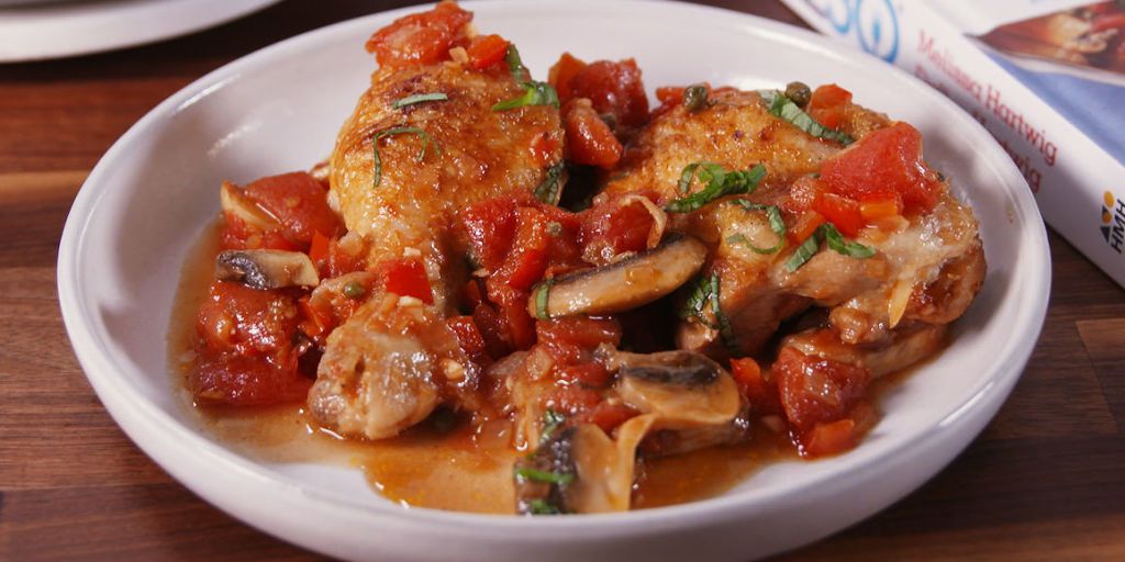 Plate of chicken with tomatoes, mushrooms, and herbs in sauce.