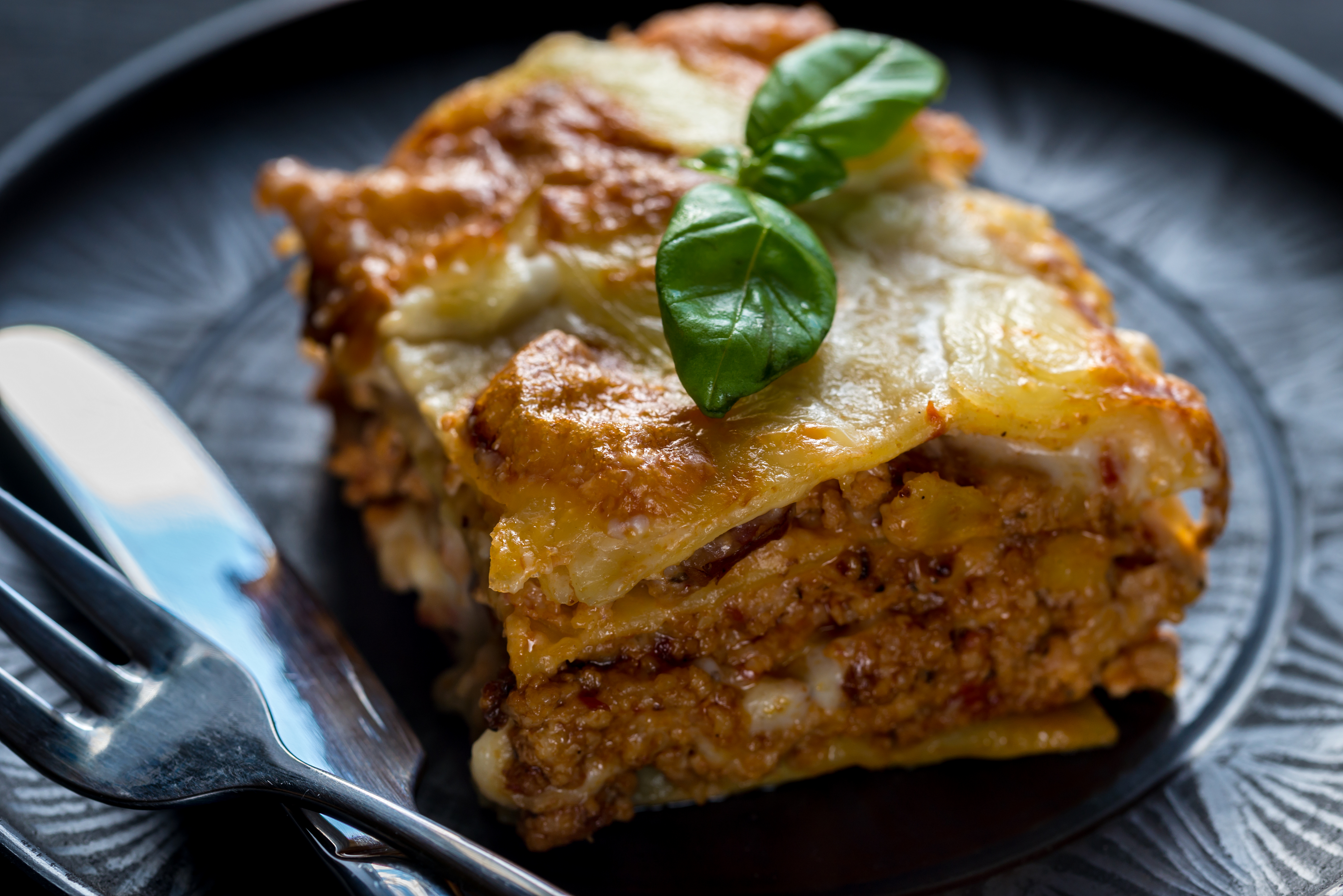A delicious slice of lasagna garnished with fresh basil on a black plate.