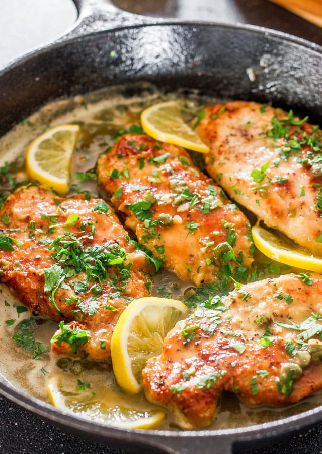 Close-up of grilled chicken breasts garnished with fresh herbs and lemon slices.