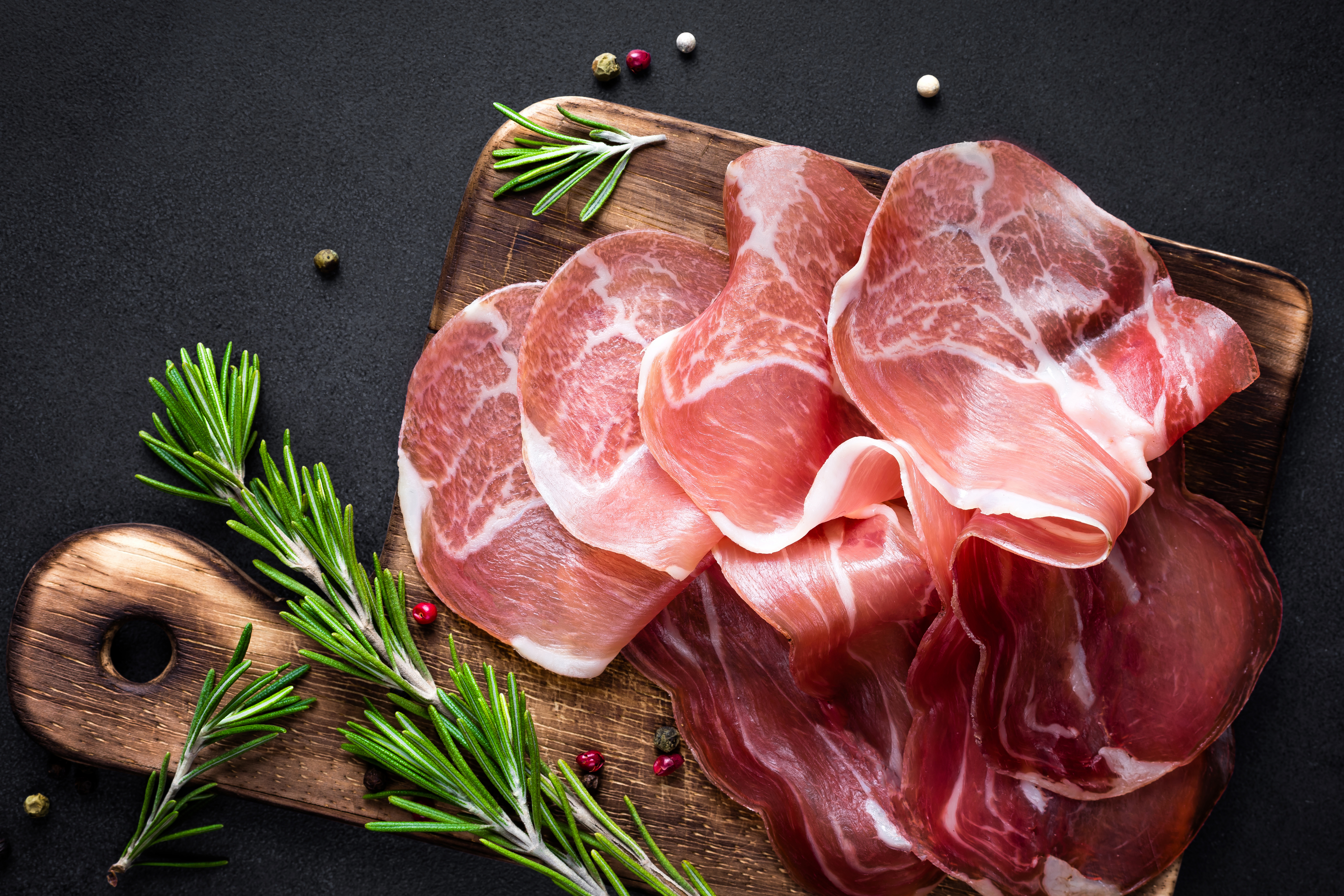 Thinly sliced prosciutto arranged on a wooden cutting board with rosemary sprigs.