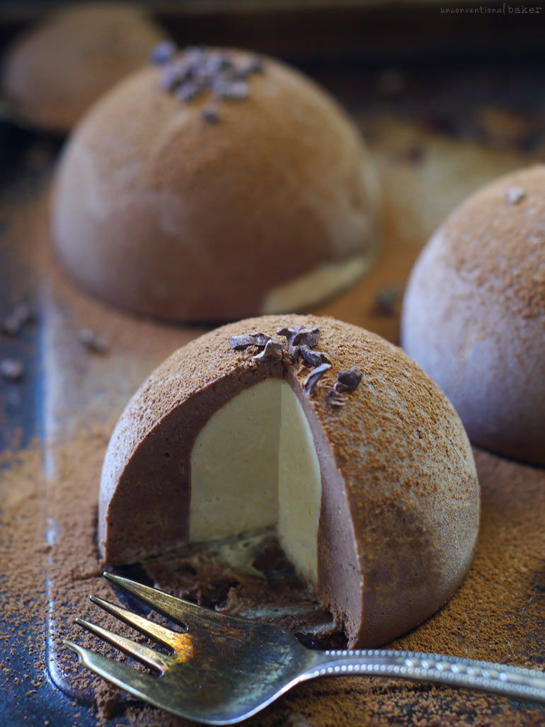 Chocolate mousse dome dessert with creamy filling and cocoa nibs on top.