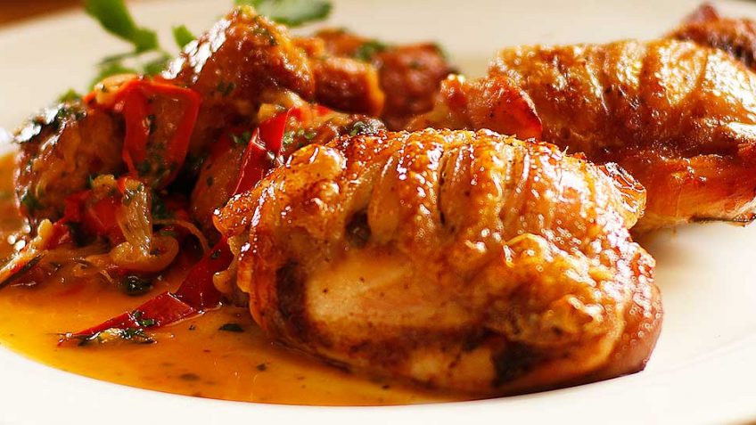 Close-up of glazed fried chicken wings with peppers and sauce.