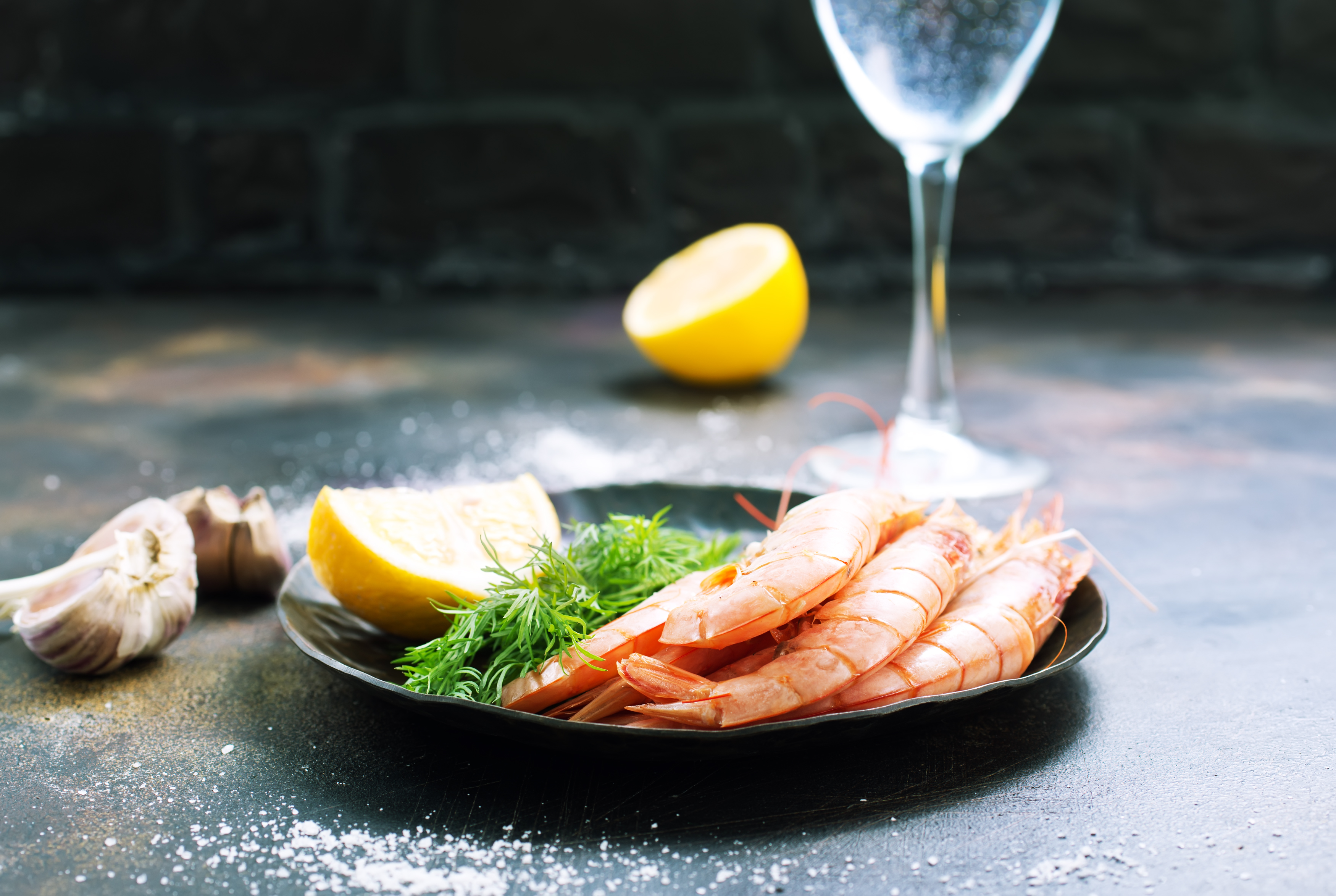 Plate of shrimp with lemon and herbs beside wine glass.