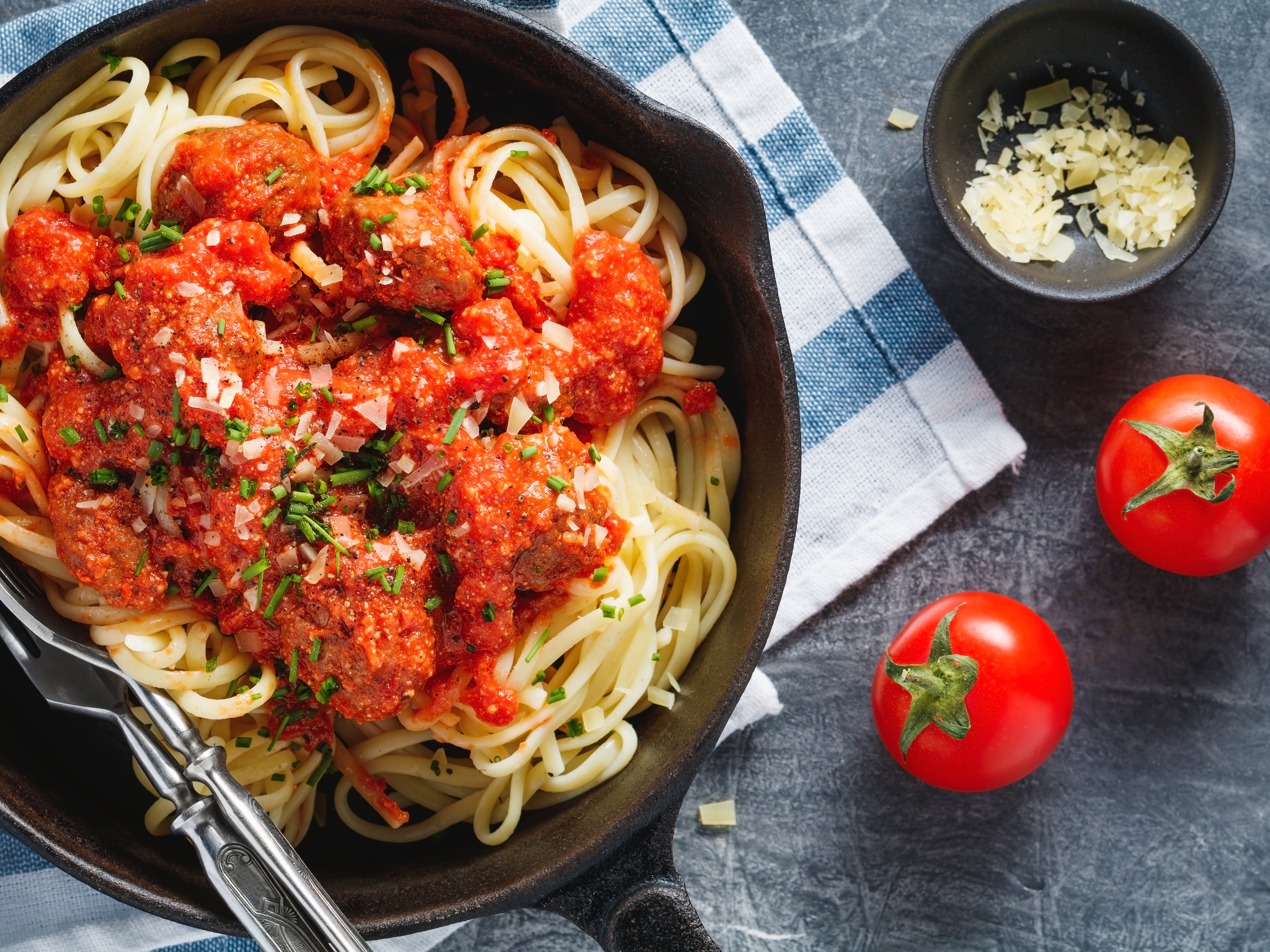 Spaghetti with meatballs and tomato sauce garnished with herbs and cheese.