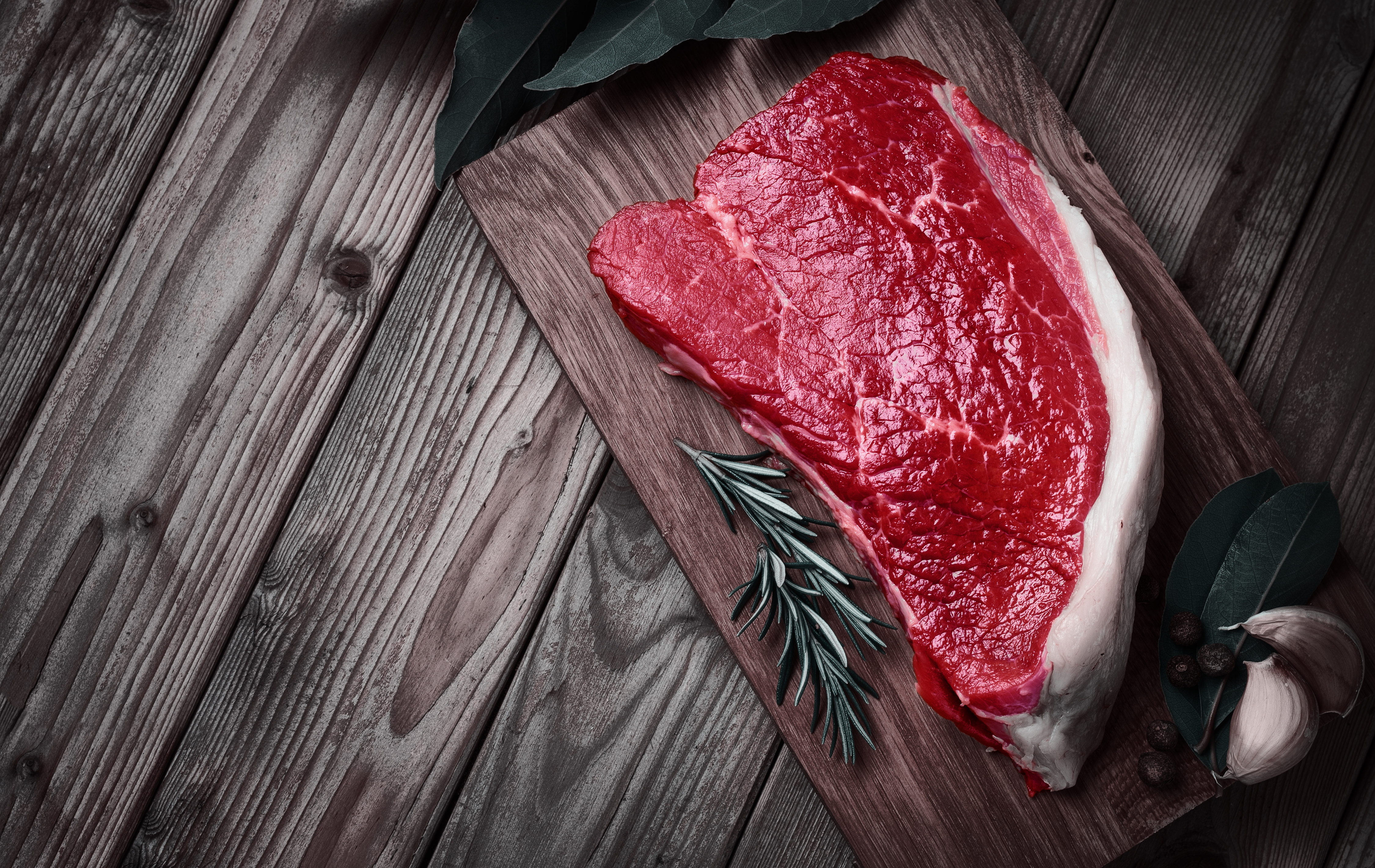 Raw beef steak on a wooden board with rosemary and garlic.