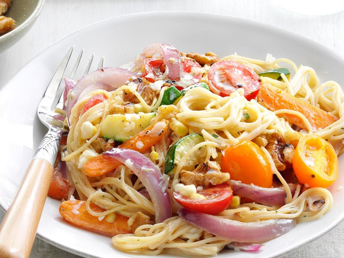 Plate of colorful vegetable pasta with cherry tomatoes and onions.