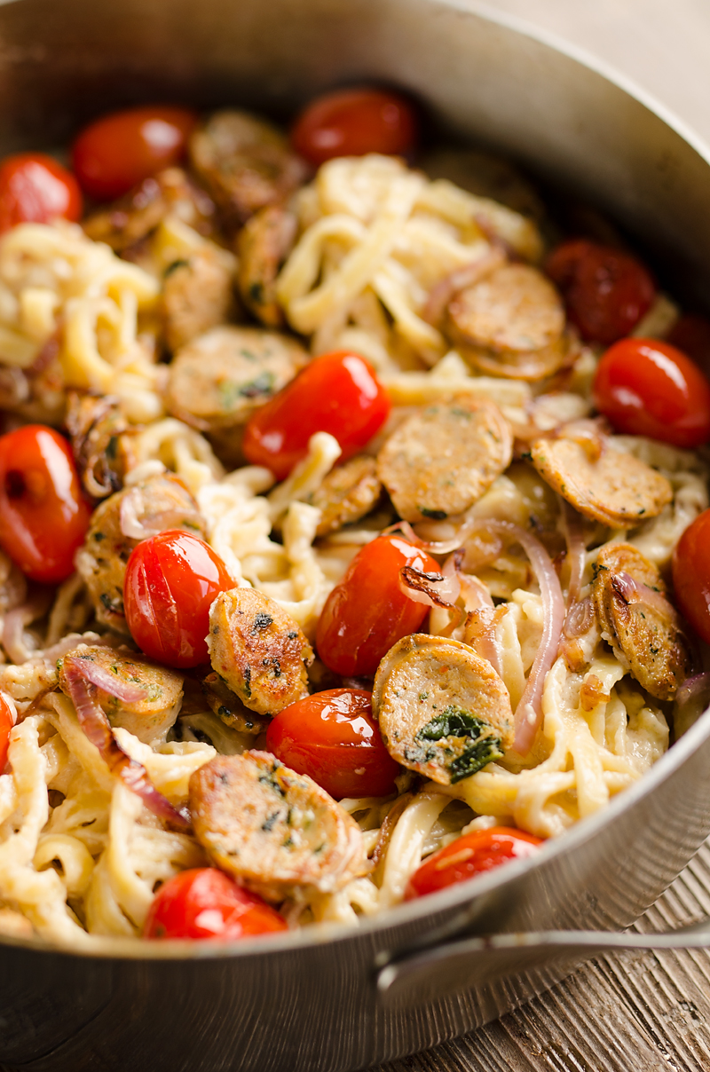 Close-up of creamy pasta with sausage slices and cherry tomatoes.