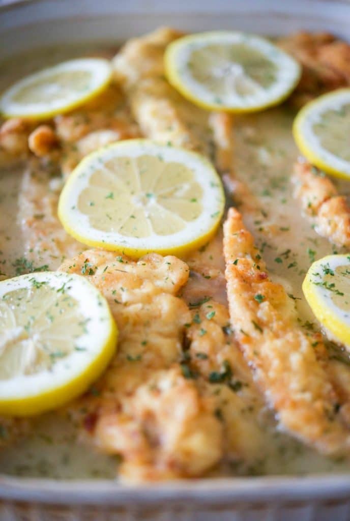 Close-up of cooked fish fillets garnished with lemon slices and herbs.