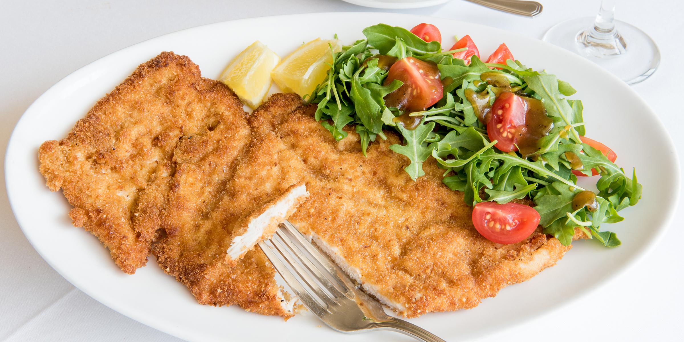 Breaded chicken cutlets served with fresh salad and lemon wedges.