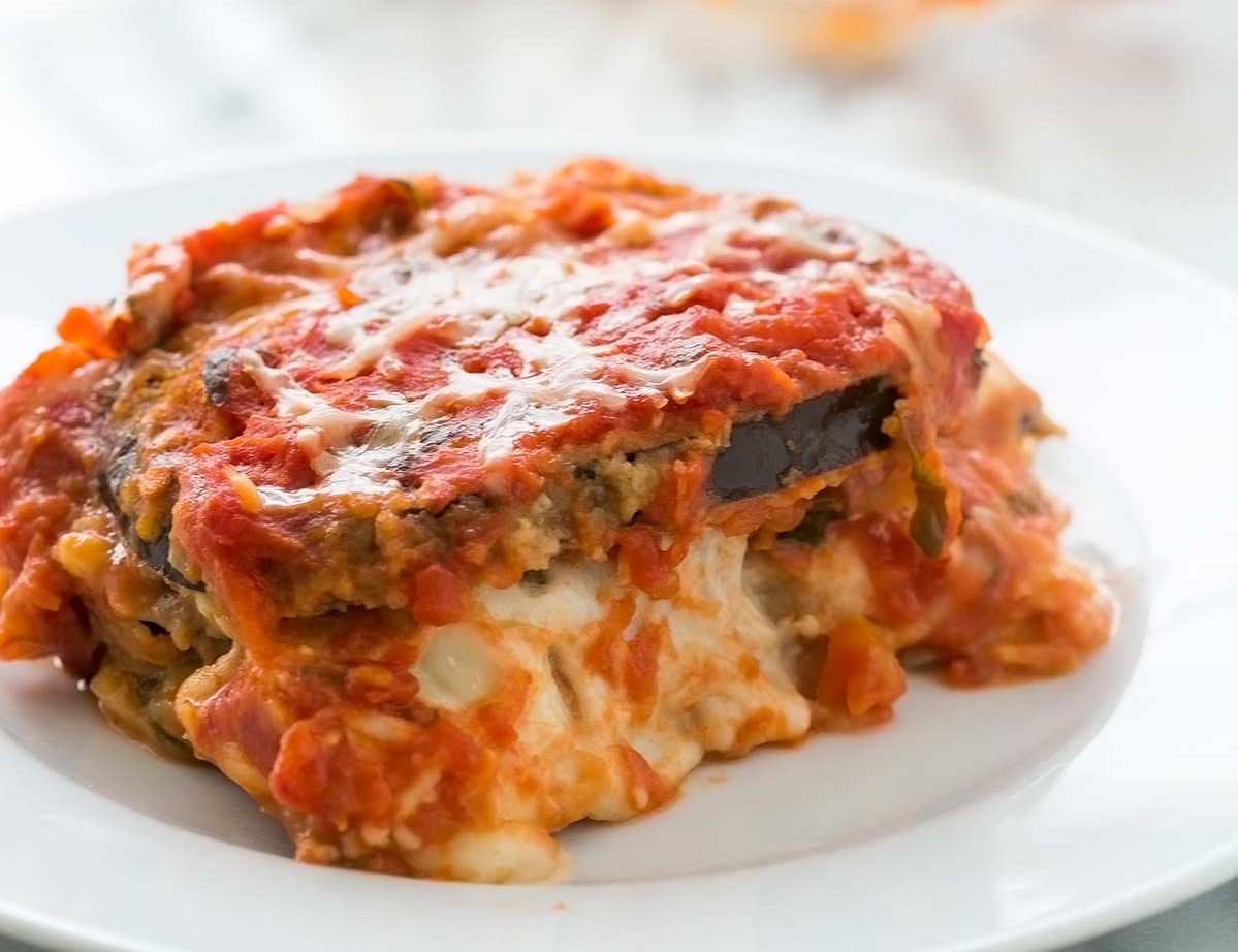 Close-up of a cheesy eggplant lasagna slice on a white plate.