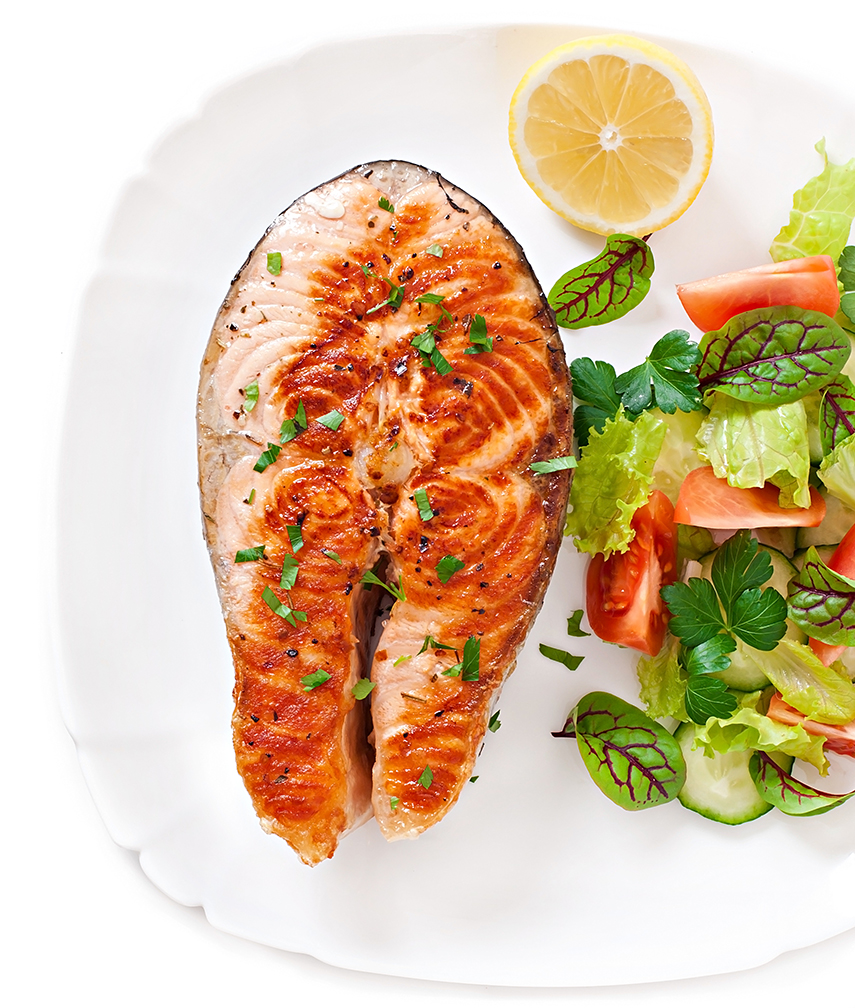 Grilled salmon steak garnished with herbs served with fresh salad.