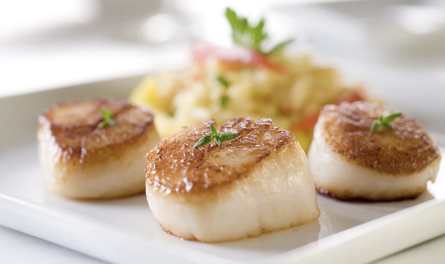 Three seared scallops garnished with herbs on a white plate.