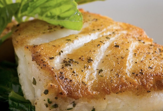 Close-up of a seasoned, grilled fish fillet on a plate.