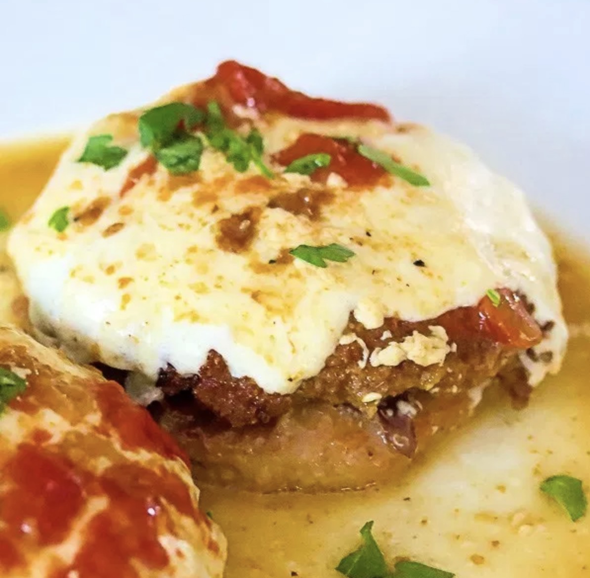 A close-up of a cheesy, baked meat dish garnished with herbs.
