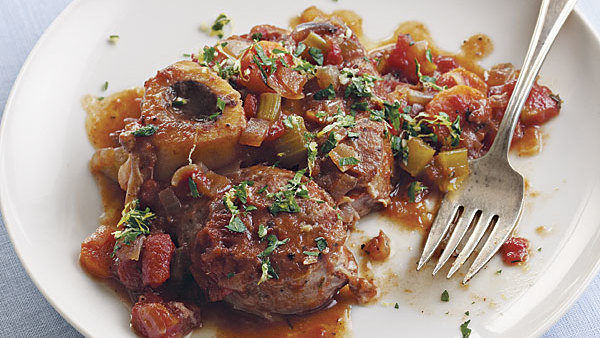 Braised meat with bone and vegetables garnished with herbs on a white plate.