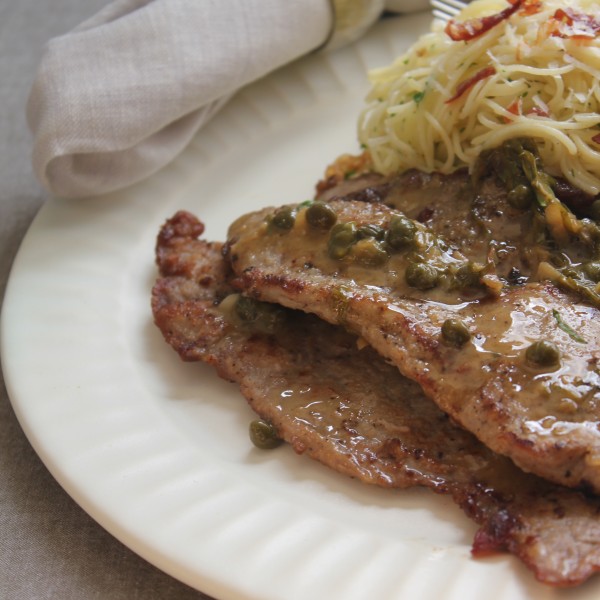 Close-up of breaded veal cutlets with creamy caper sauce on a white plate.