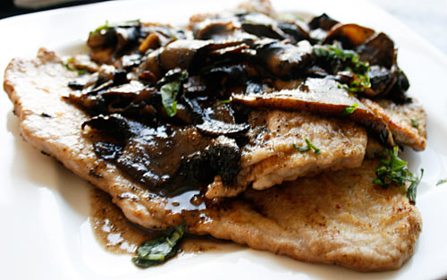 Sautéed chicken breast topped with mushrooms and herbs on a white plate.